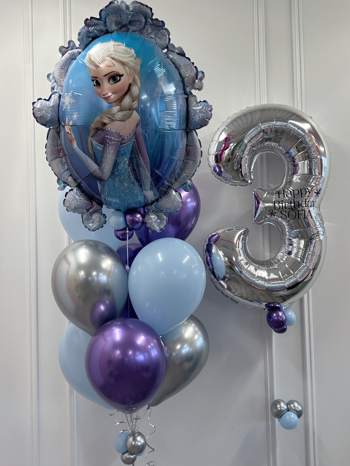 Close-up of Frozen Elsa birthday balloons featuring an Elsa supershape foil balloon, silver number 3 with personalized birthday message and coordinating blue, purple and silver latex balloons.