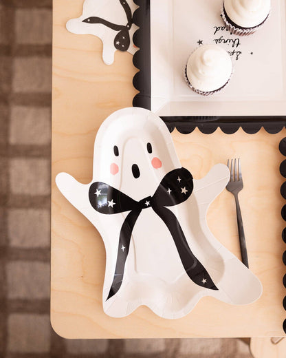 Ghost-shaped plate with a black bow on a wooden surface