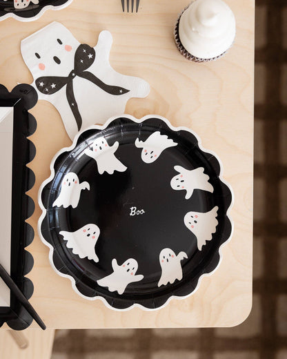 Black paper plate with white ghost designs and 'Boo' text on a wooden surface.