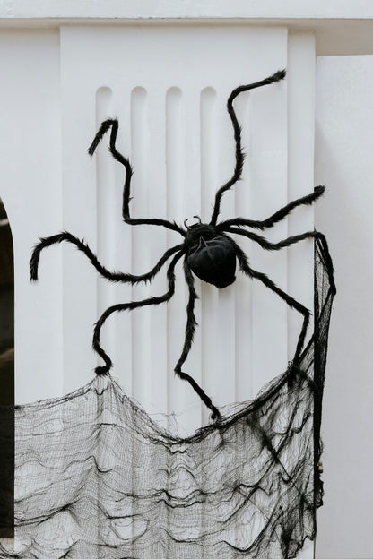 Giant black spider decoration posed on a white wall with black webbing, Halloween indoor and outdoor prop. Available in Toronto or Canada-wide.