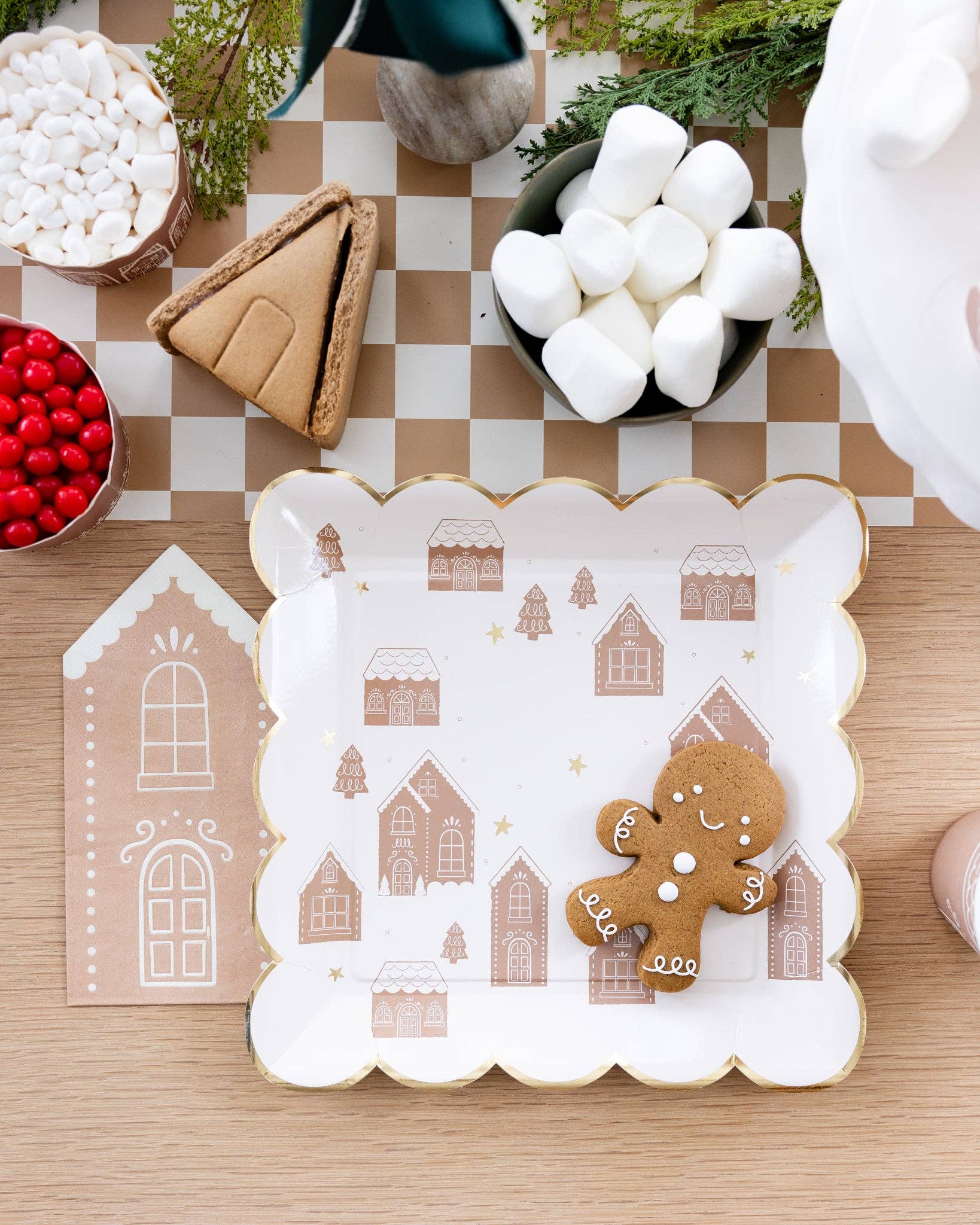 Decorative plate with gingerbread house pattern on a checkered tablecloth with holiday items.