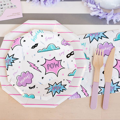 Pink superhero-themed plate and napkins paired with two-tone purple wooden culery.