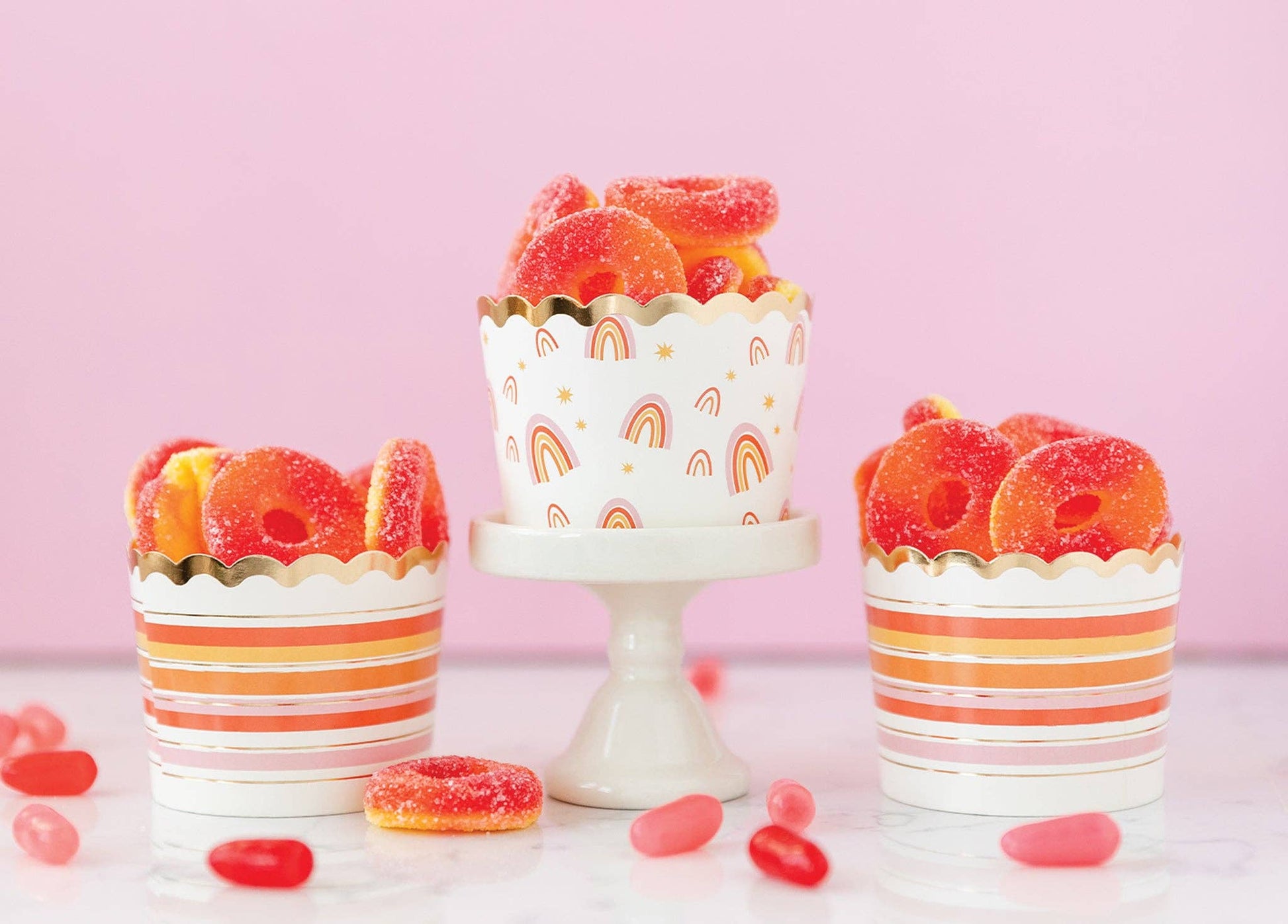 Decorative rainbow food cups with gummy candies on a pink background