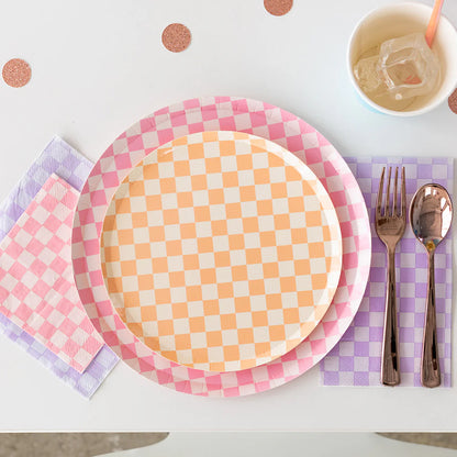 Close-up of a peach checkered dessert plate layered over pink and lavender partyware, styled with rose gold cutlery and glittery table confetti.