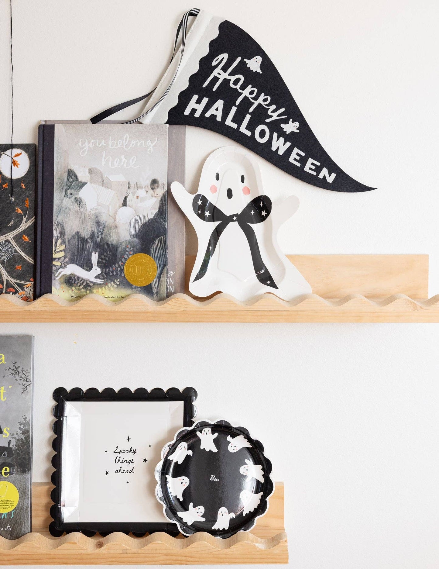 Decorative Halloween shelf with ghost figurine, books, and banner on a white wall.