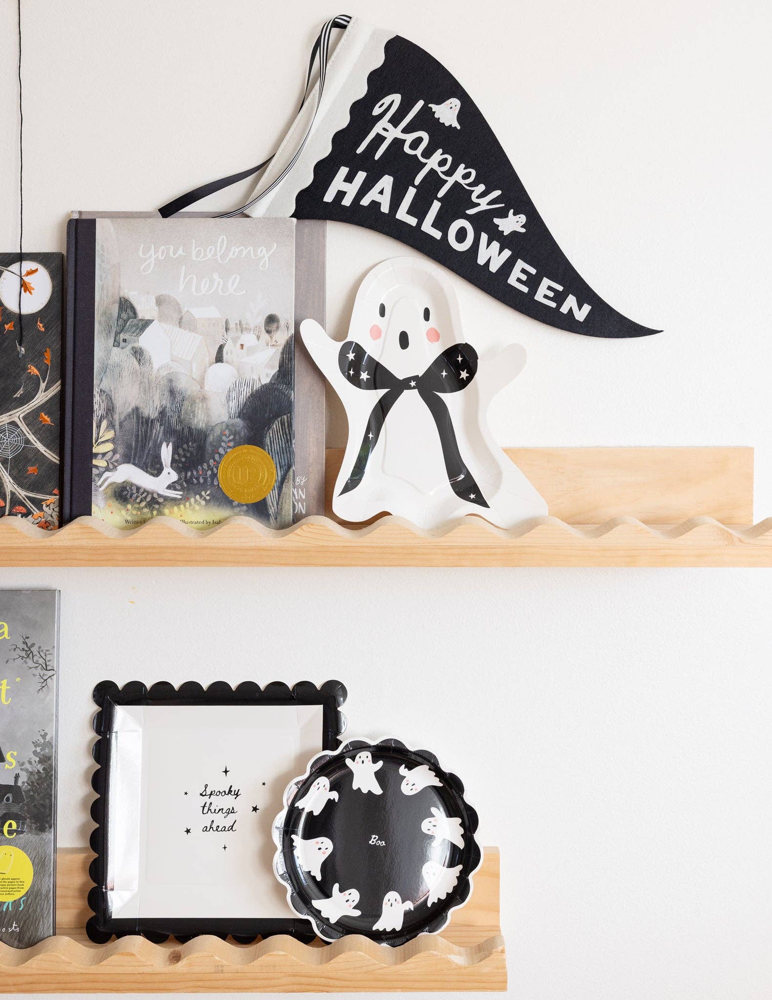 Decorative Halloween shelf with ghost figurine, books, and banner on a white wall.