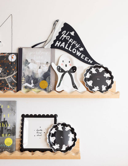 Halloween-themed decor items on a shelf including books, a ghost figurine, and decorative plates.