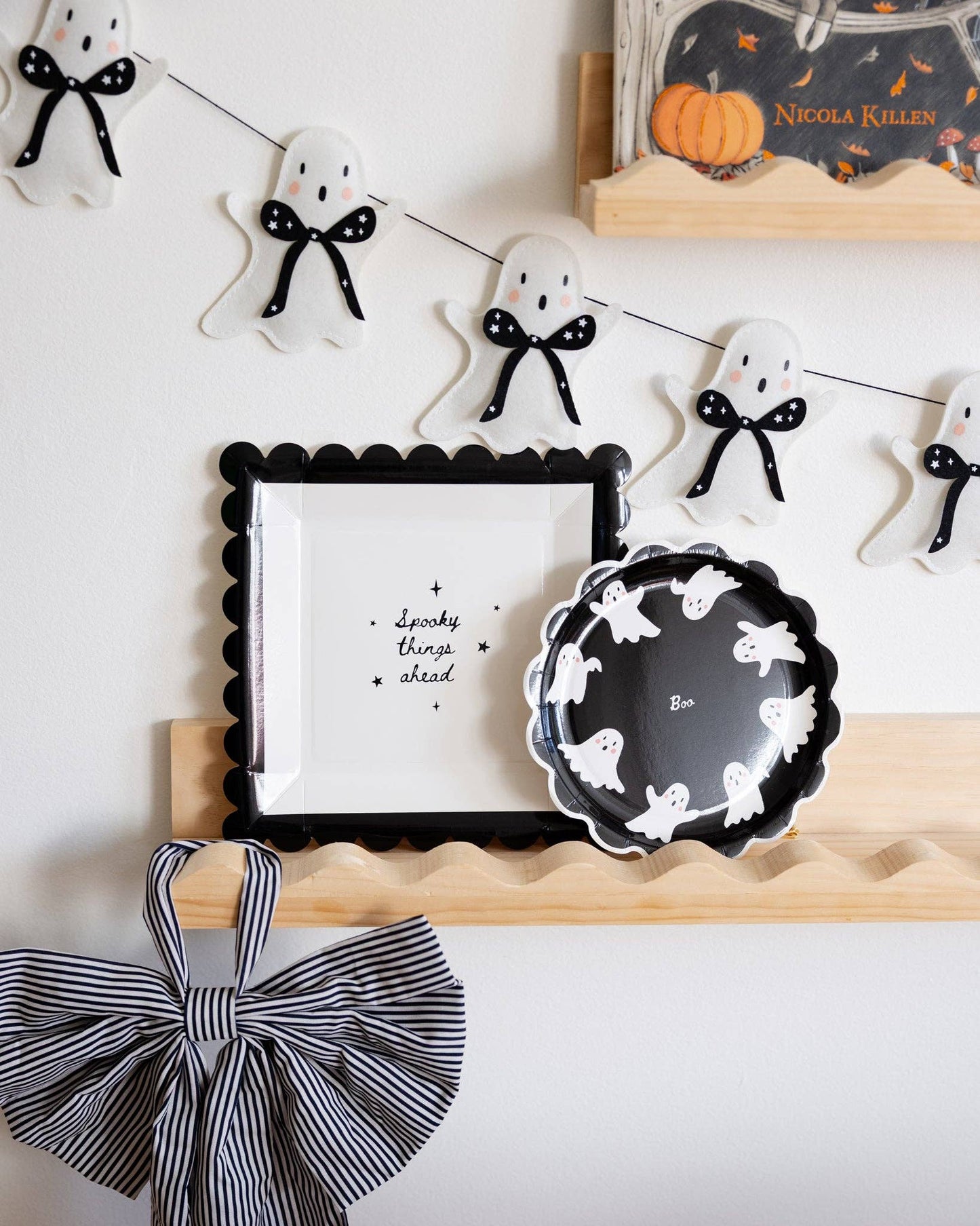 Halloween-themed decor with ghost decorations, a framed picture, and a plate on a white wall.