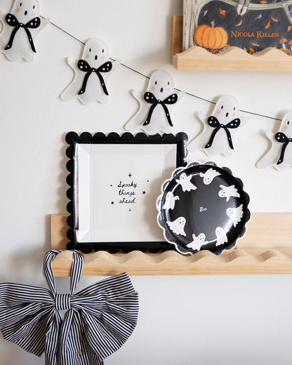 Halloween-themed decor with ghost decorations, a framed picture, and a plate on a white wall.