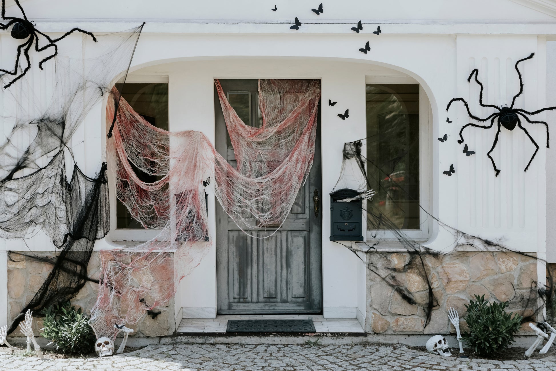 Halloween house exterior decorated with giant black spiders, webs, and skeleton props.