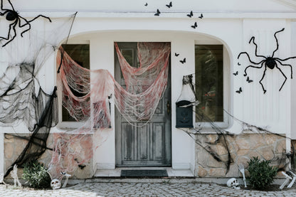 Halloween house exterior decorated with giant black spiders, webs, and skeleton props.