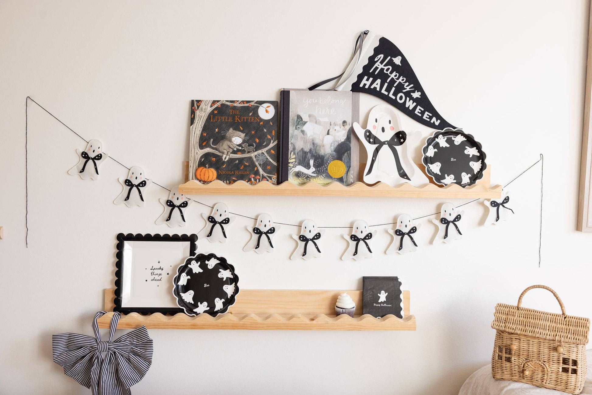 Decorative shelf with Halloween-themed items including books, plates, and a banner on a white wall.