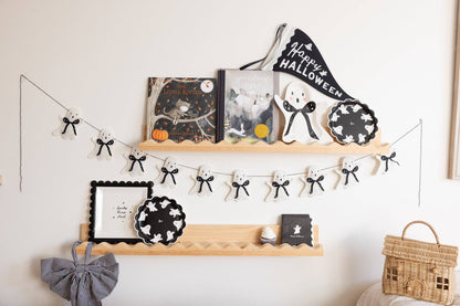 Decorative shelf with Halloween-themed items including books, plates, and a banner on a white wall.