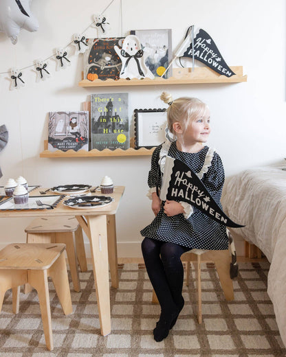 Child holding a 'Happy Halloween' banner in a room decorated for the holiday.
