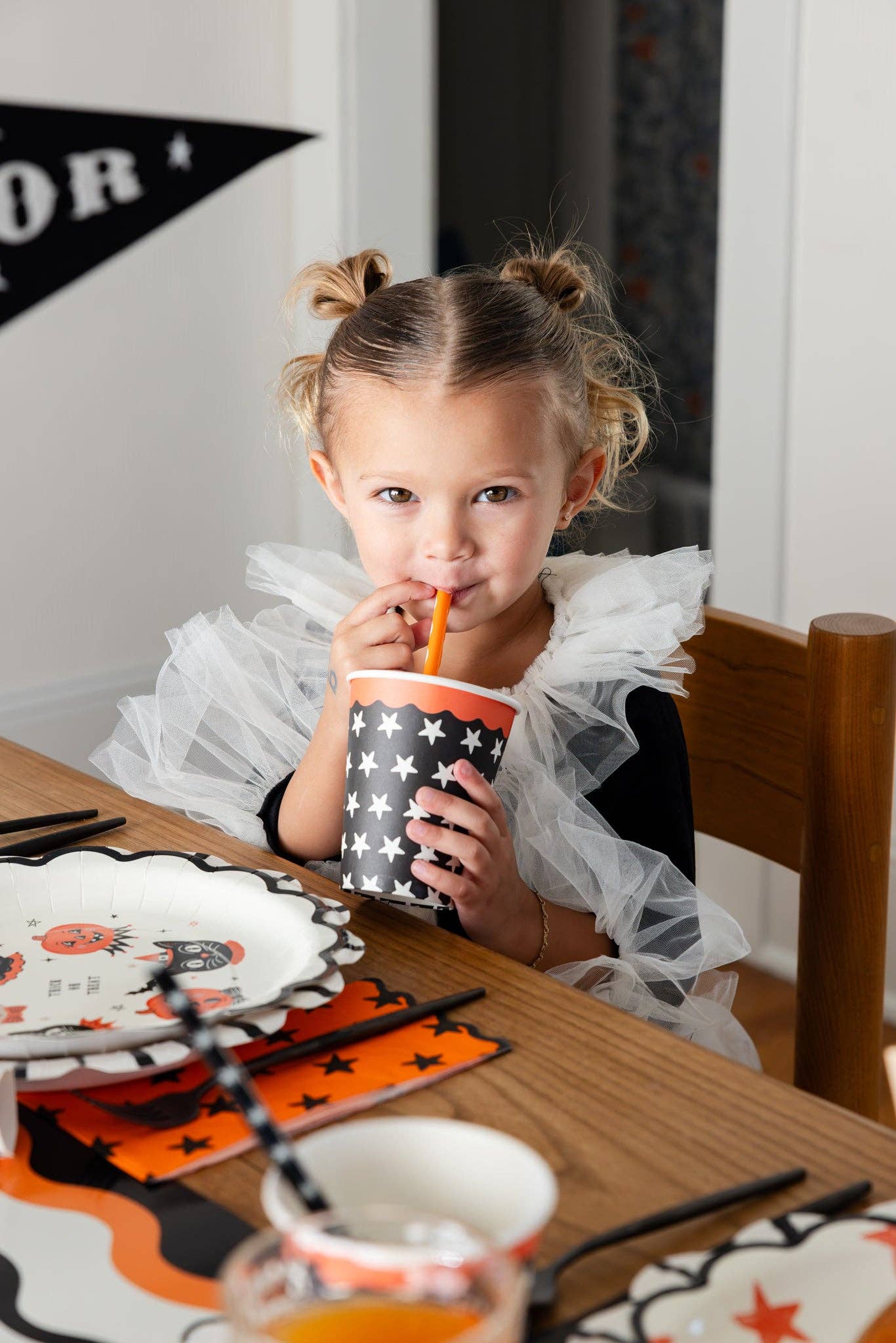 Child drinking from a Halloween-themed cup at a dining table.