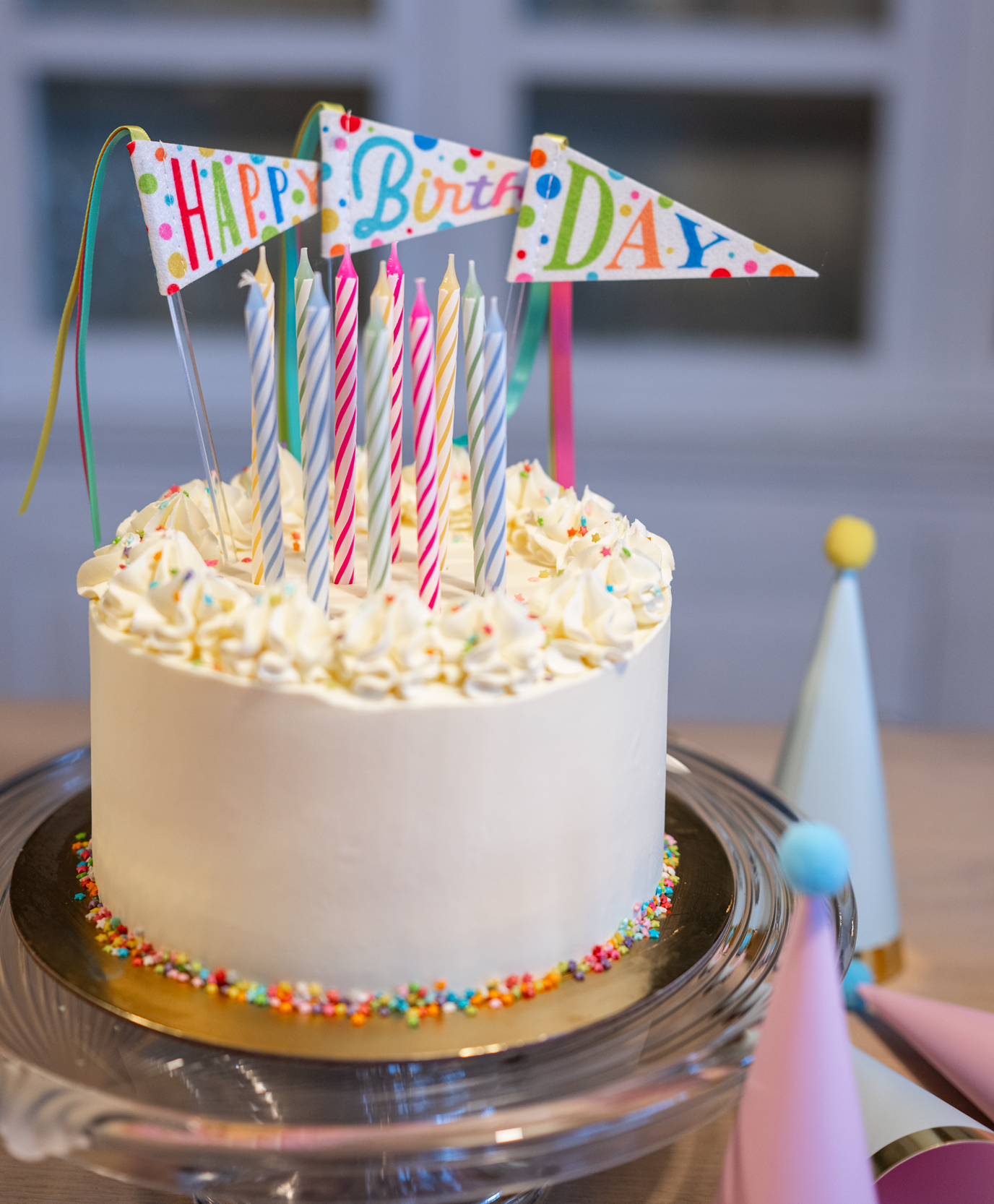 Birthday cake with candles and 'Happy Birthday' flags on a table.