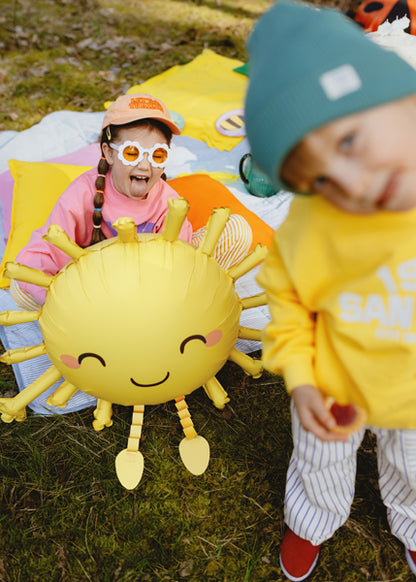 Two children playing outdoors with a sun-shaped inflatable balloon