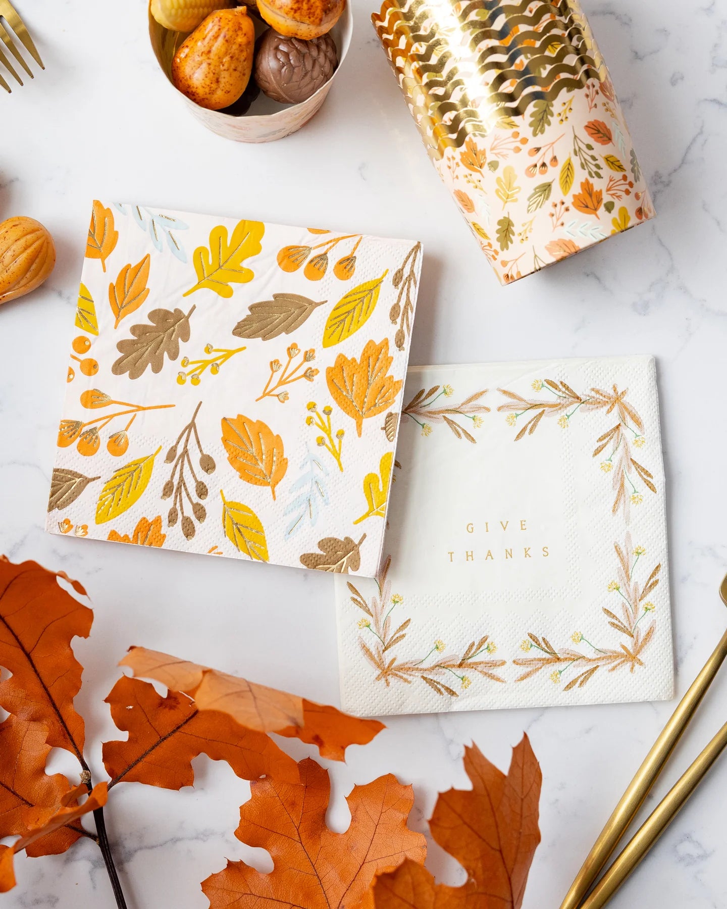 Two napkins with autumn leaf patterns on a marble surface with fall leaves and gold accents sold in Toronto