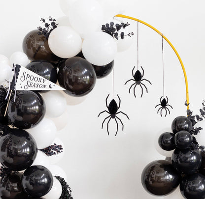 Halloween balloon garland decoration with black and white balloons, black spider cutouts hanging from a yellow arch, and a small 'Spooky Season' banner.