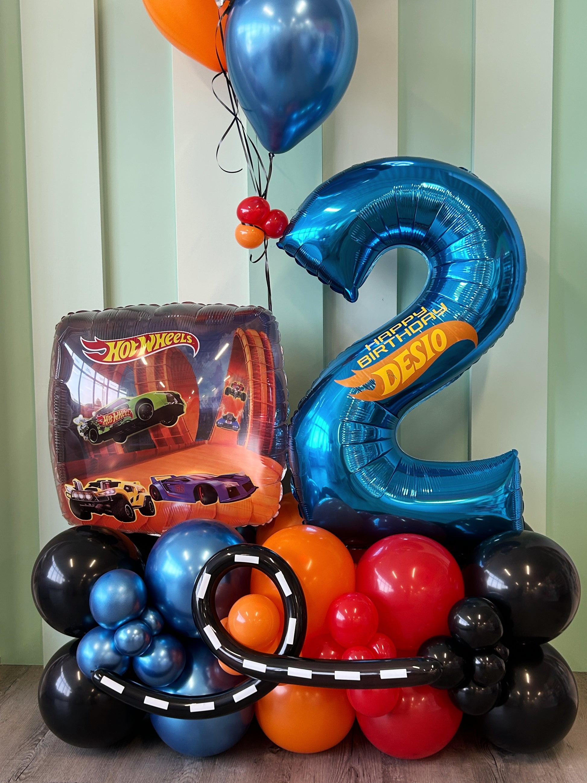 Colorful balloon arrangement with a number '2' and Hot Wheels theme against a striped background