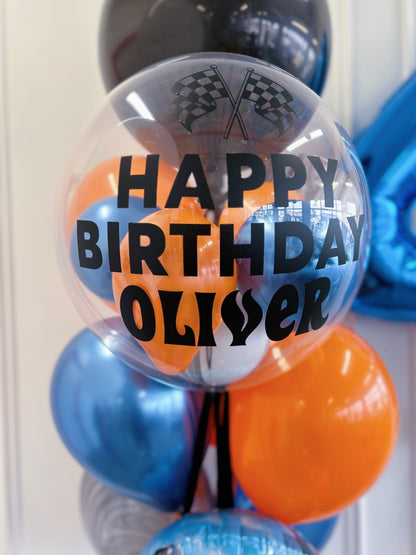 Personalized racing birthday bubble balloon with blue, orange, black + silver balloons and checkered flags.