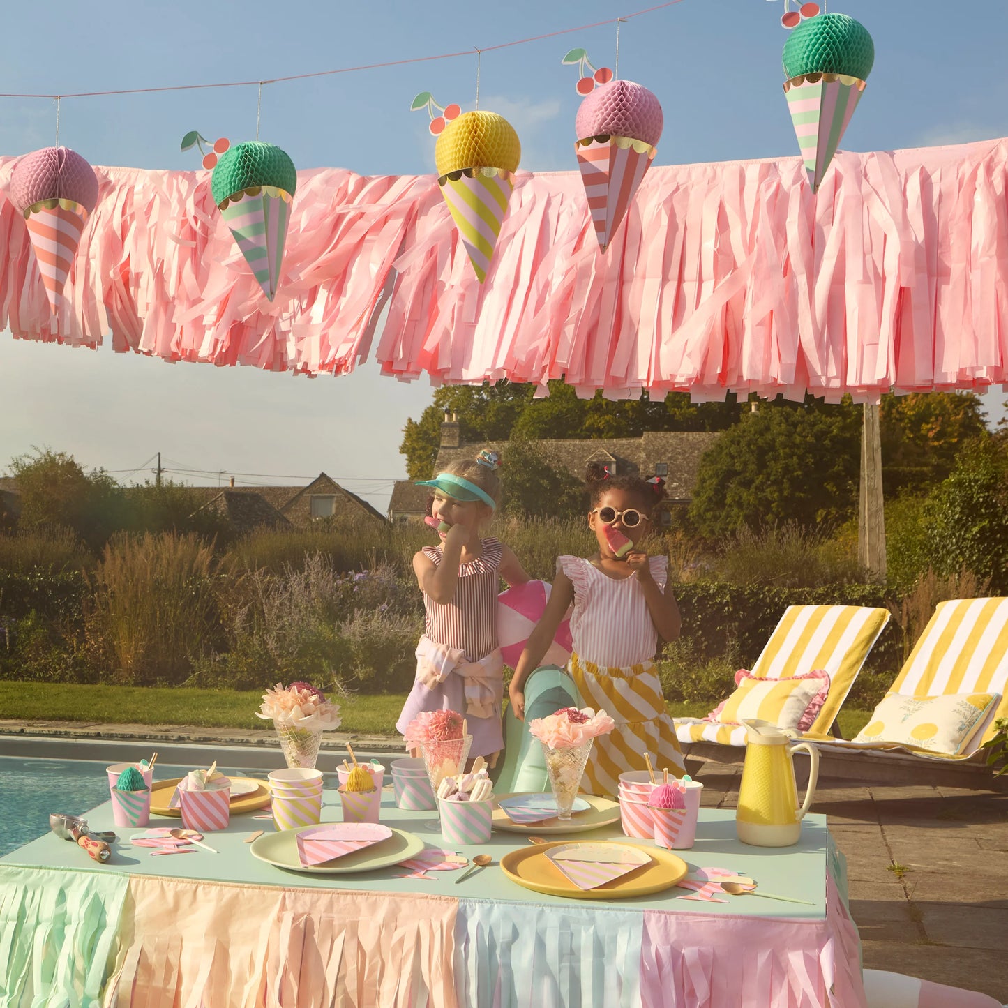 Ice cream-themed kids party with pastel cups, tassel garland, and hanging cone decorations by the pool