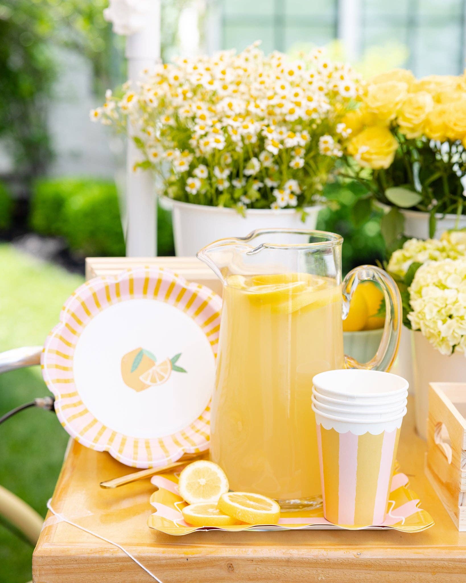 Toronto summer setup with yellow and pink striped paper cups surrounded by fresh lemons and lemonade pitcher.