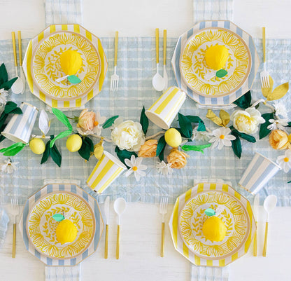 Decorative table setting with lemon-themed plates, flowers, and cutlery on a checkered tablecloth.