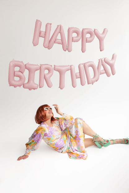 matte light pink 'happy birthday' letter balloons with model posing in front 