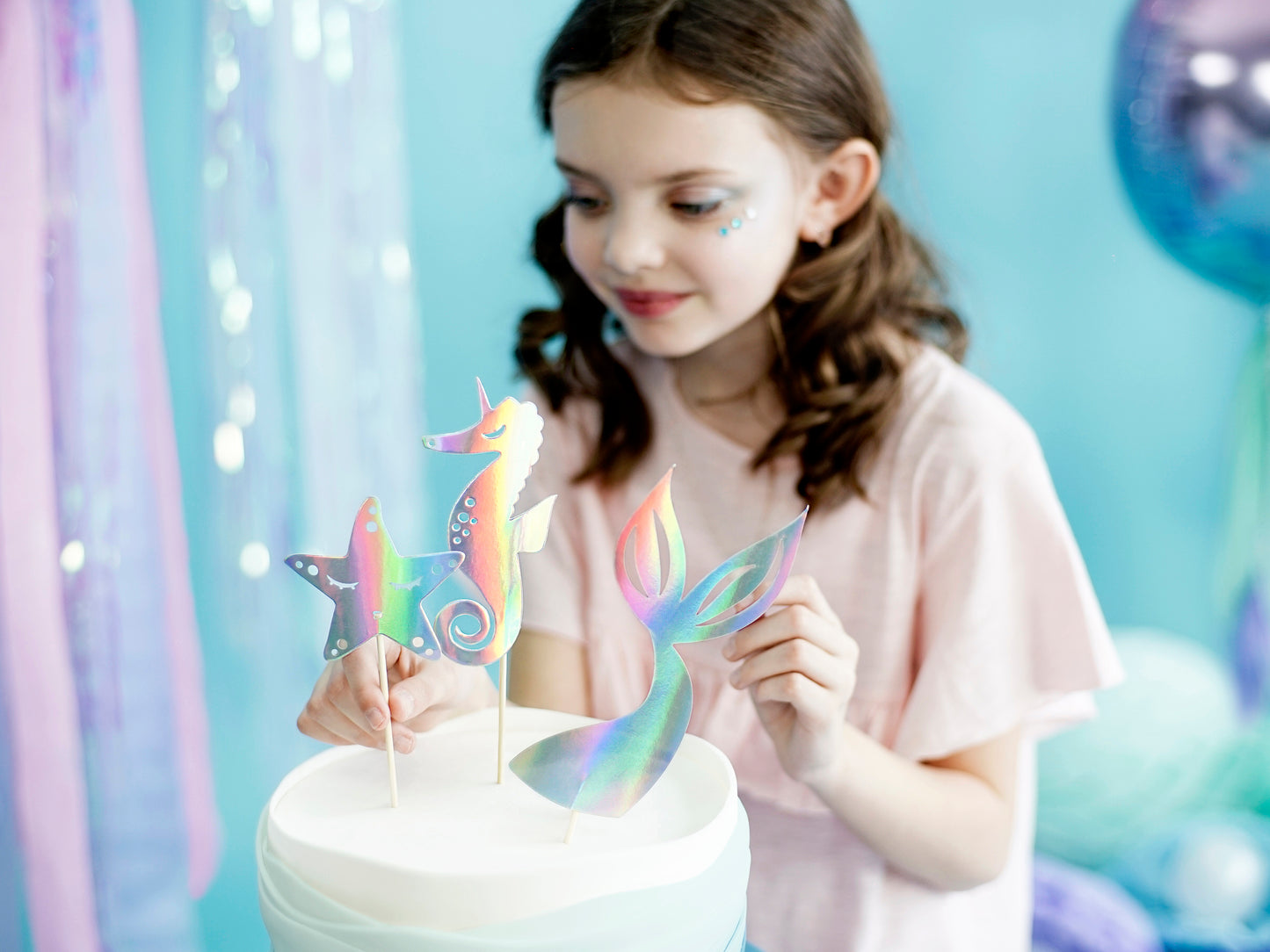 girl placing mermaid themed cake toppers on a birthday cake