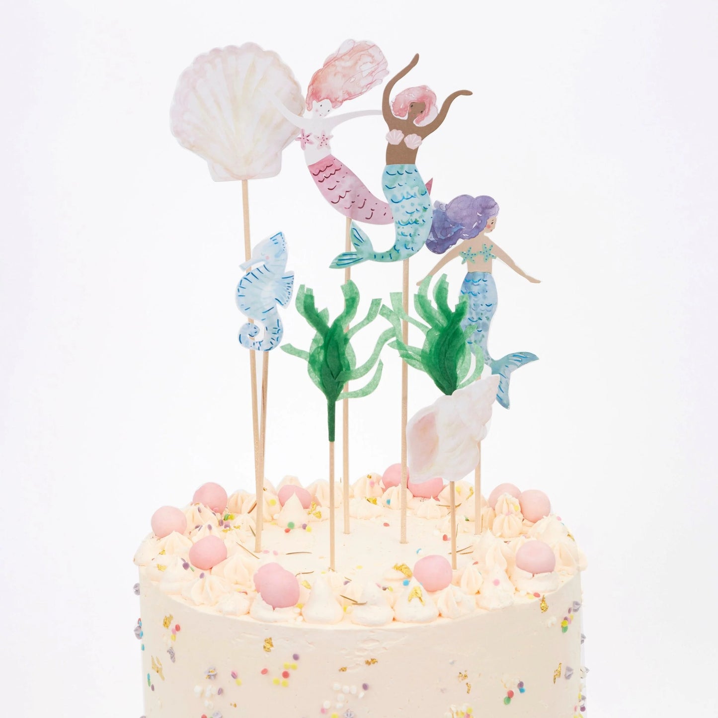 Pastel-colored mermaid-themed cake toppers on a white cake with colorful sprinkles.