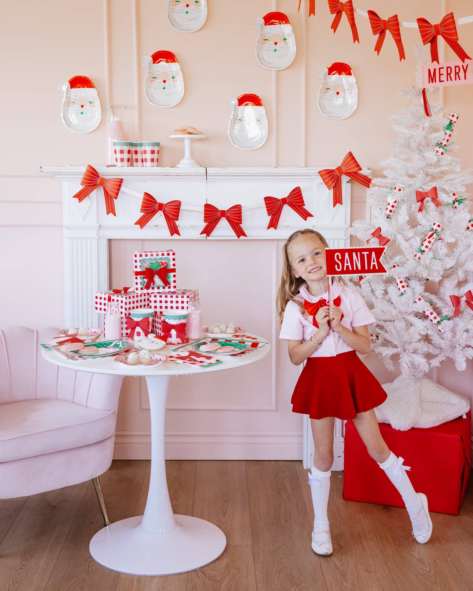 Child holding Santa felt pennant in festive holiday setup with Christmas table and tree.
