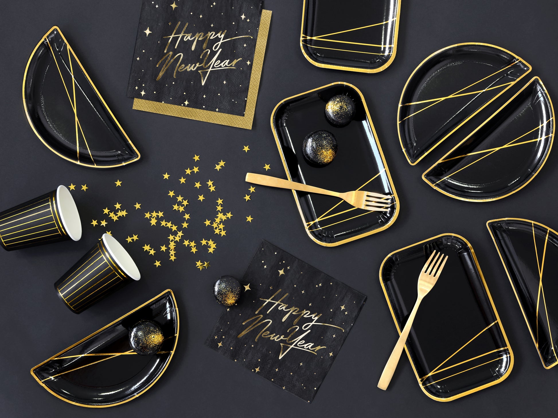 Metallic gold star confetti scattered across black New Year’s Eve table setting with matching plates and cups.