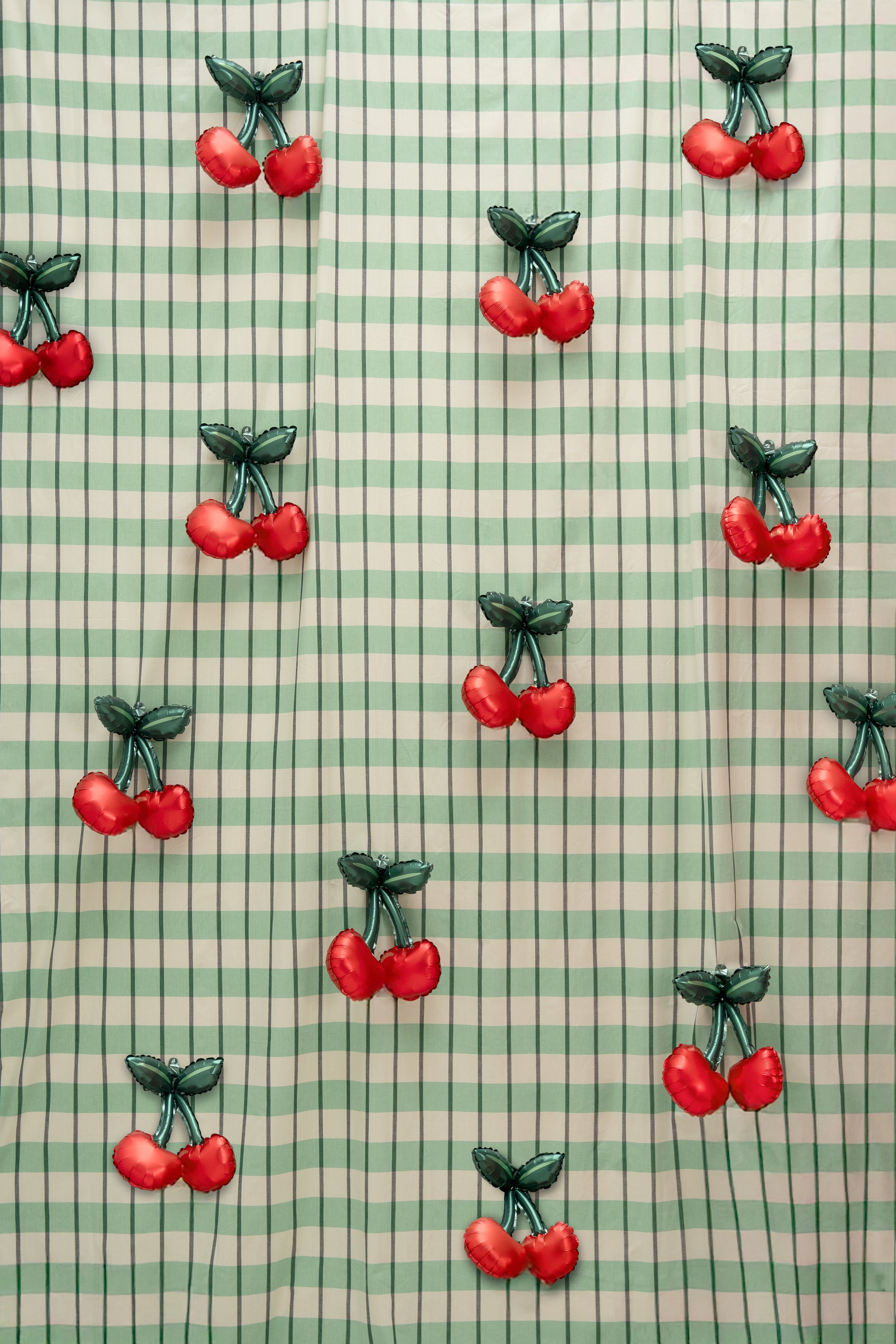 Cherry foil balloon wall backdrop with mini cherry balloons on green gingham, perfect for Toronto parties and photo booths.