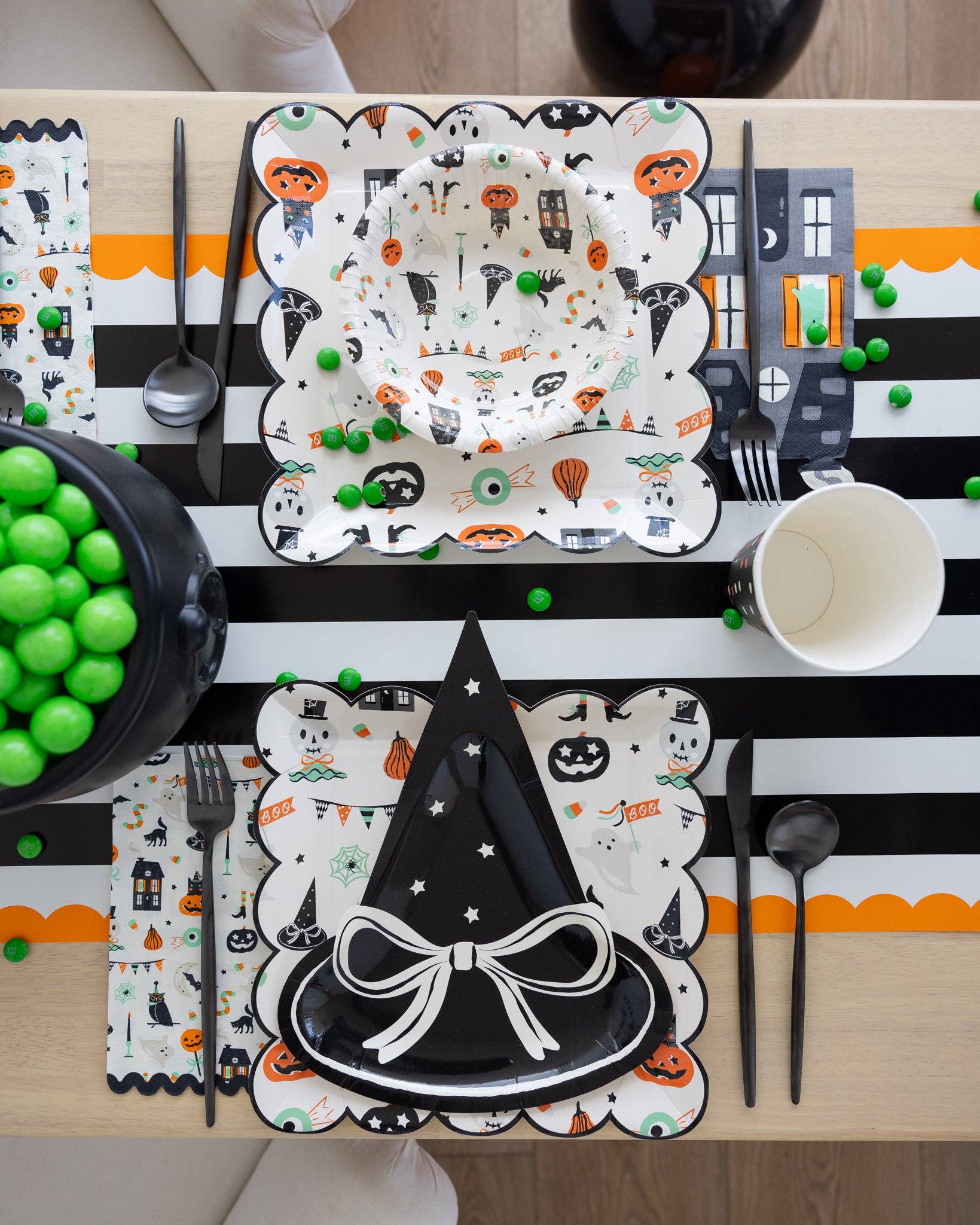 Halloween-themed table setting with decorative plates, napkins, and cutlery on a striped tablecloth.