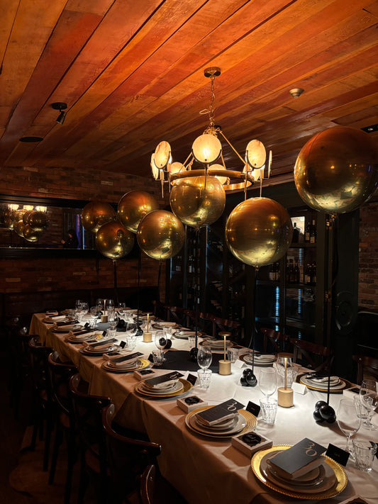 Gold Orbz balloon centerpieces on black stands styled along a New Year’s dinner table available for pick up or delivery in Toronto.