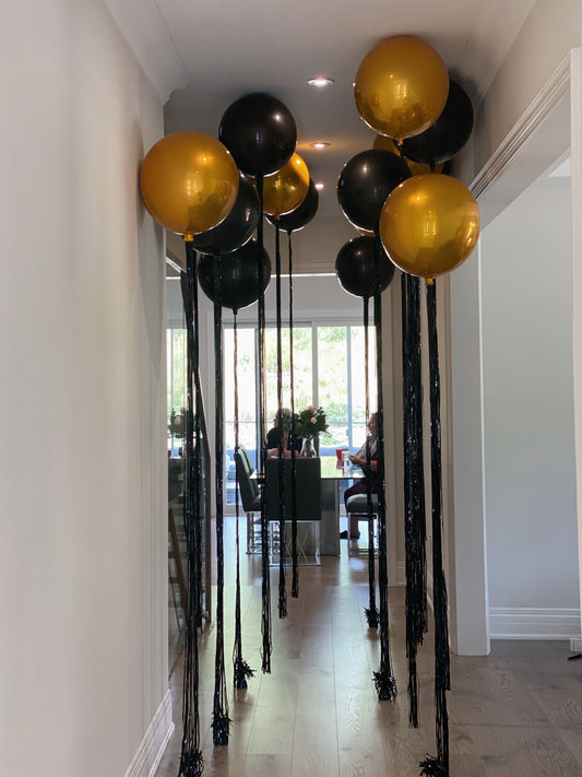 Black + gold, Orbz helium balloons with black tassels floating along a hallway ceiling for a New Year’s Eve celebration in Toronto.