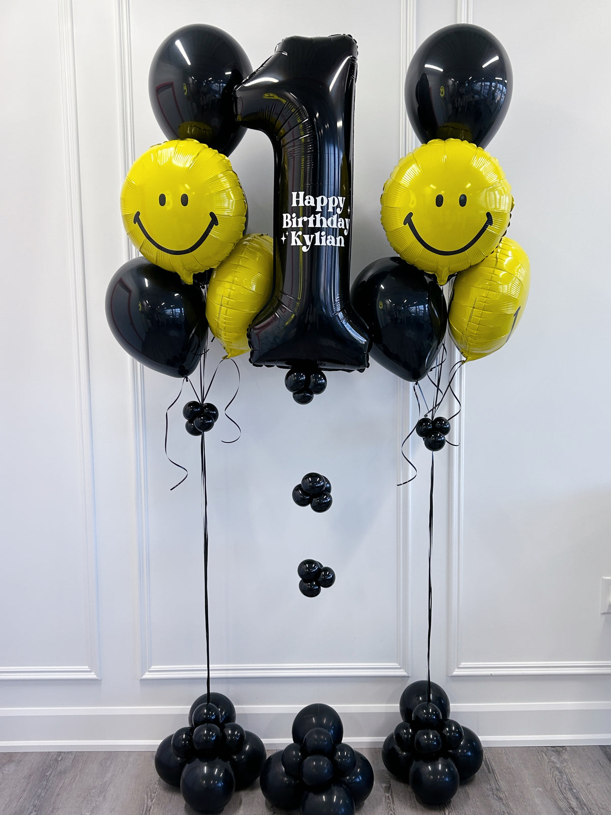 One Happy Dude black + yellow birthday balloon package with personalized number balloon, smiley face balloons + weighted bases in Toronto.