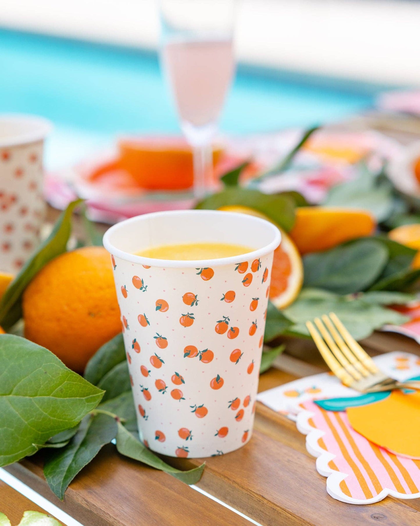 Paper cup with orange pattern on a table with oranges and green leaves