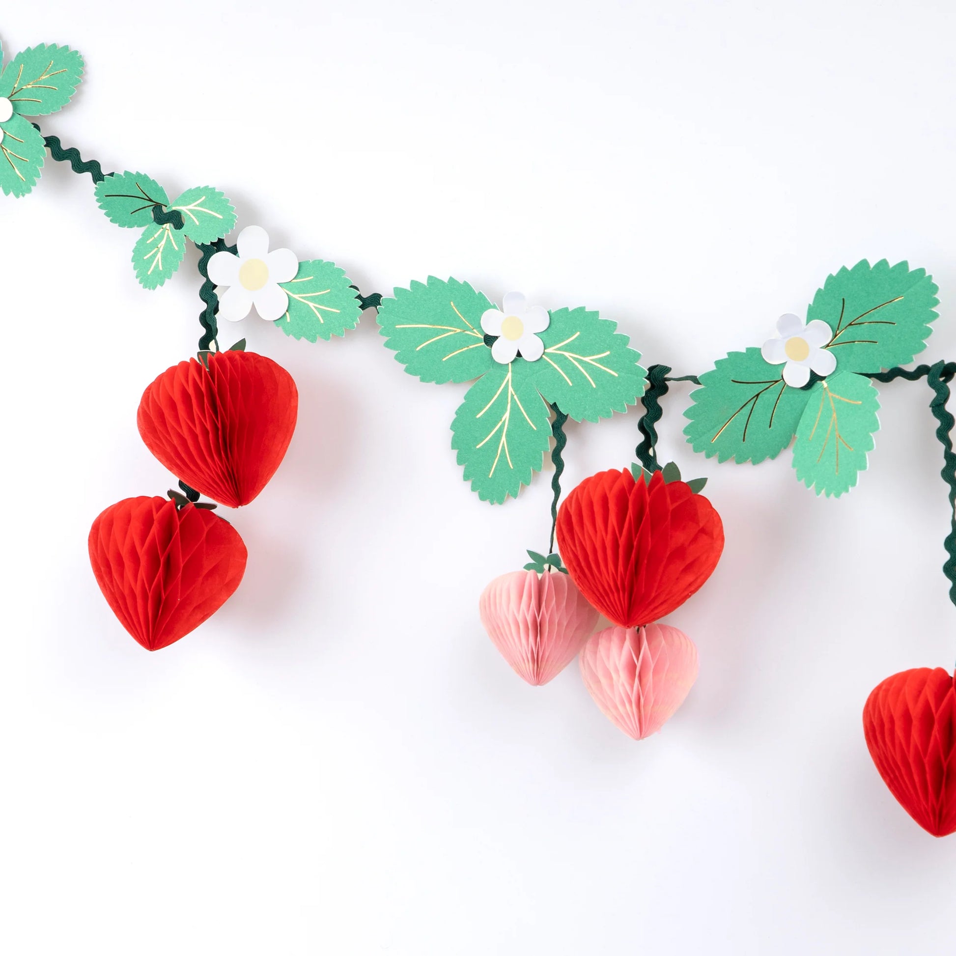 Close-up of strawberry honeycomb garland with green leaves and white flower cutouts