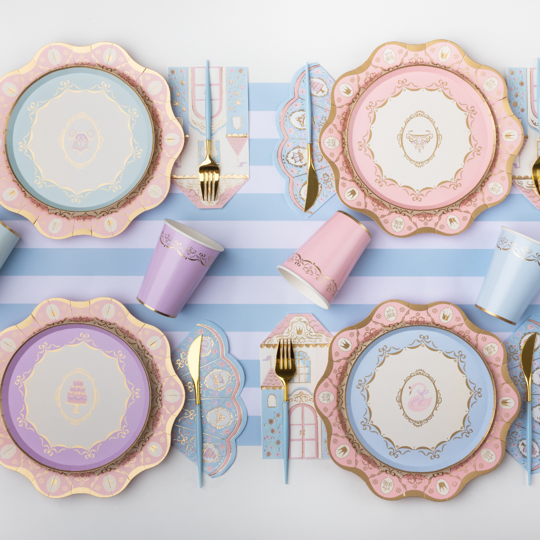 Pastel Parisian princess party table setting with castle napkins, scalloped plates, cups and gold cutlery.