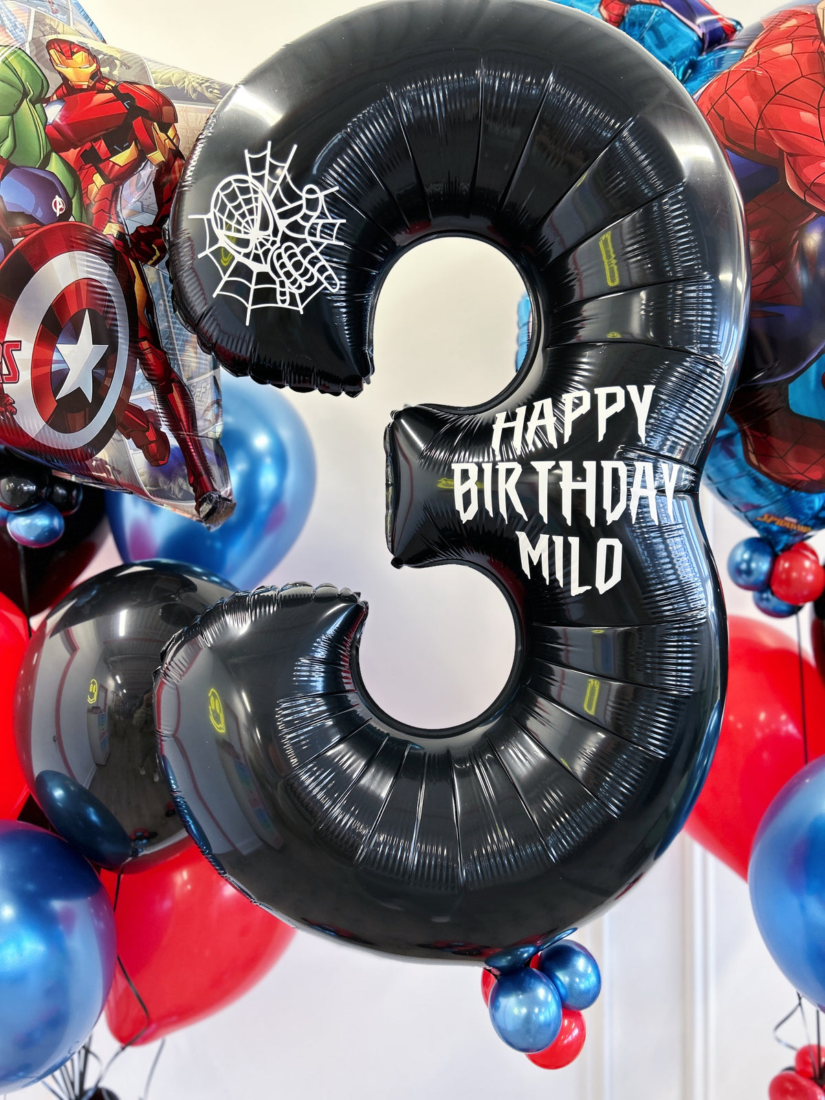 Personalized black number birthday balloon with superhero web detail, surrounded by red, blue + black balloons in Toronto.