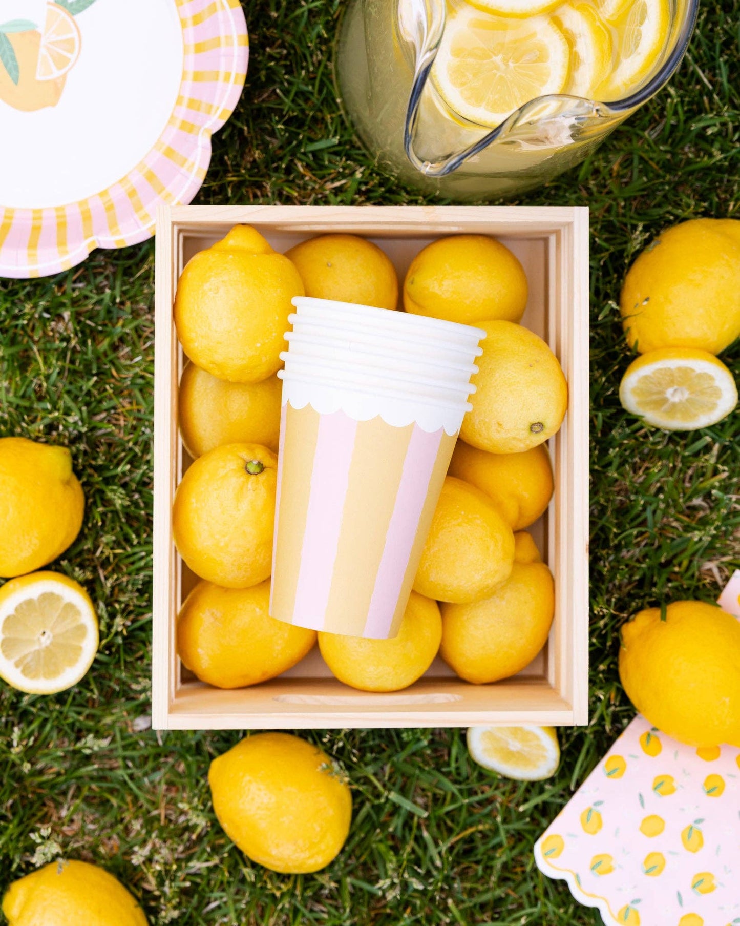 Box of lemons with a pitcher of lemonade on grass