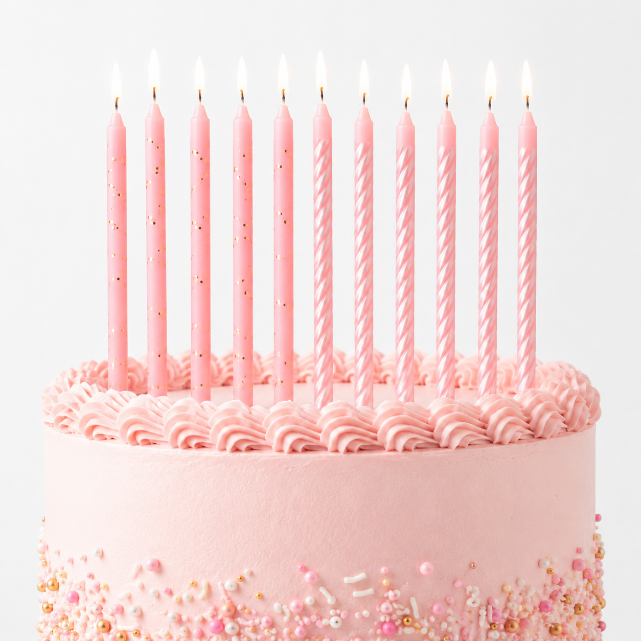 A pink frosted birthday cake with ten lit pink taper candles on top, decorated with sprinkles around the base, against a clean white background.
