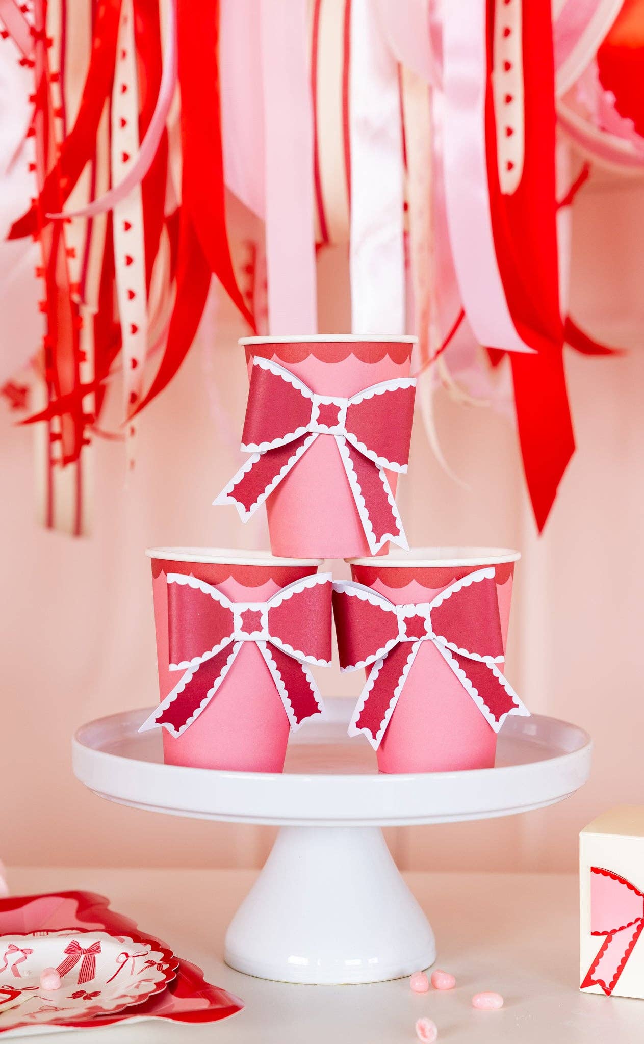 Pink bow party cups styled on a white cake stand for a Valentine’s Day celebration, available in Toronto at Confetti My Party