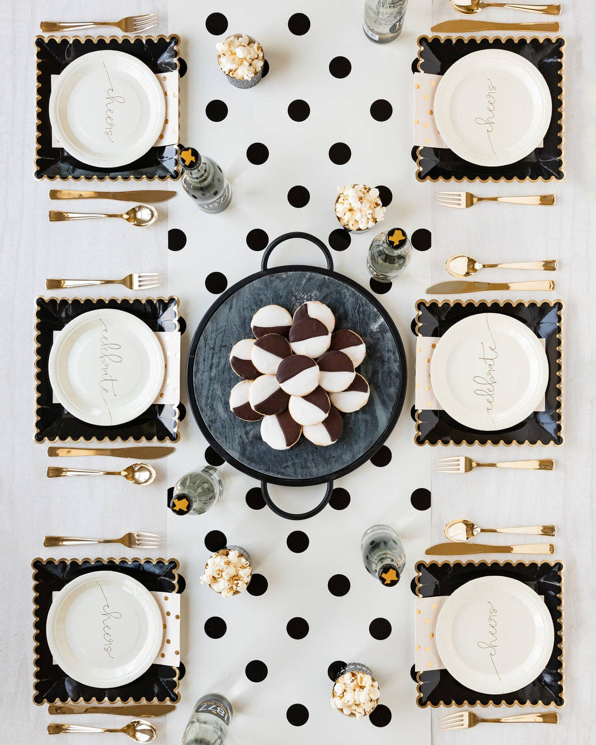 Elegant table setting with black and white polka dot placemats, gold cutlery, and decorative cookies.