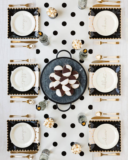 Elegant table setting with black and white polka dot placemats, gold cutlery, and decorative cookies.