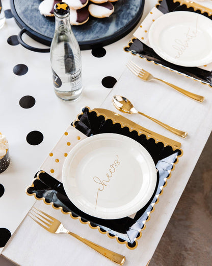 Table setting with black and white plates, gold cutlery, and decorative elements on a polka dot table runner