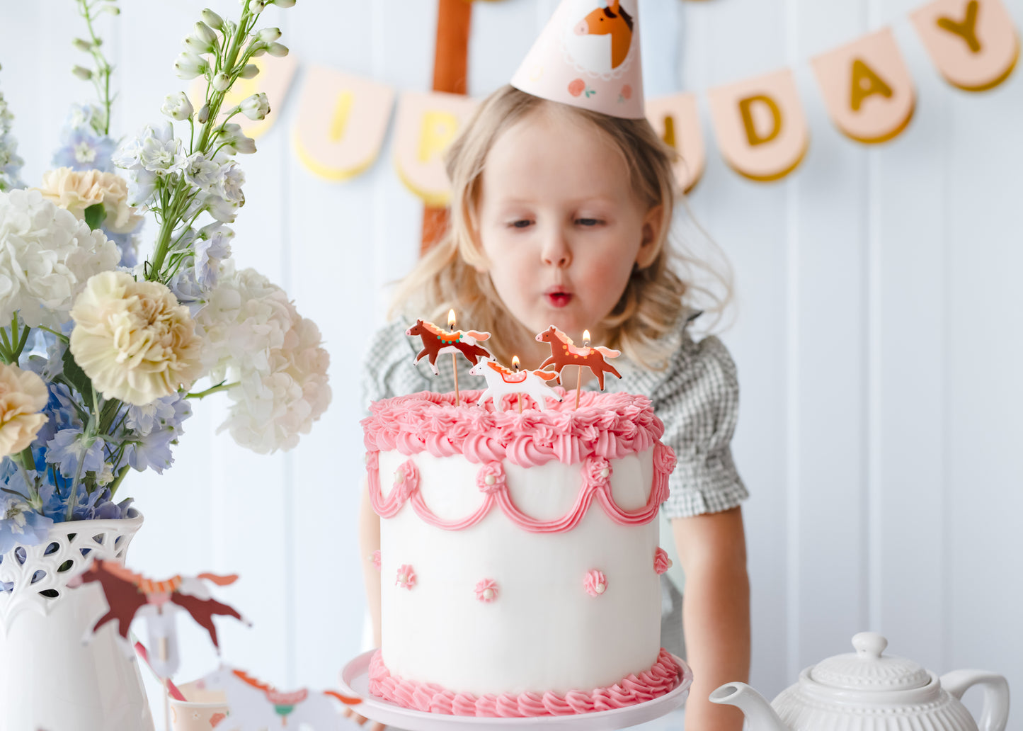 Child blowing out pony-shaped birthday candles on a pink frosted cake, sold at Confetti My Party Toronto