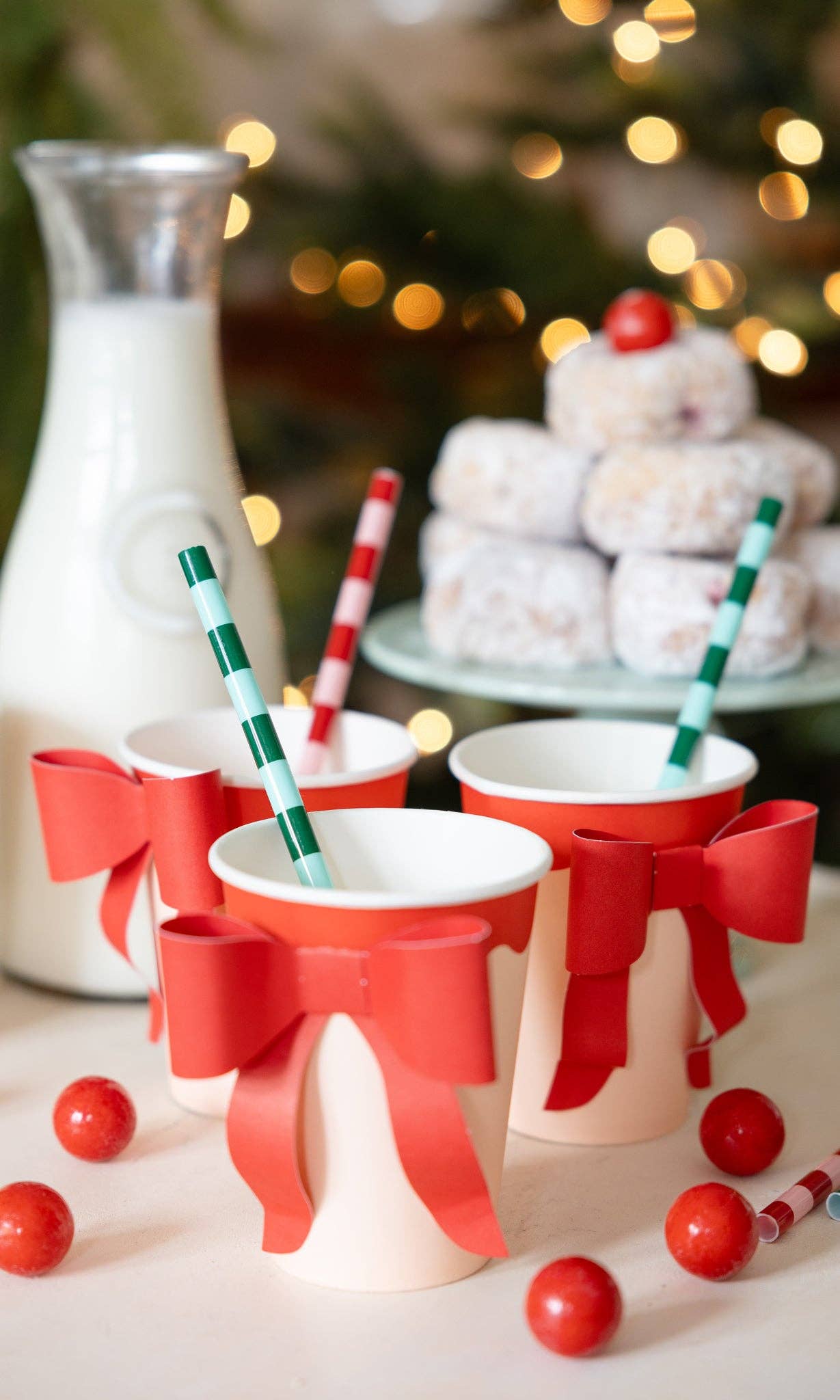 Set of Christmas-themed cups with red bows and straws on a festive background.